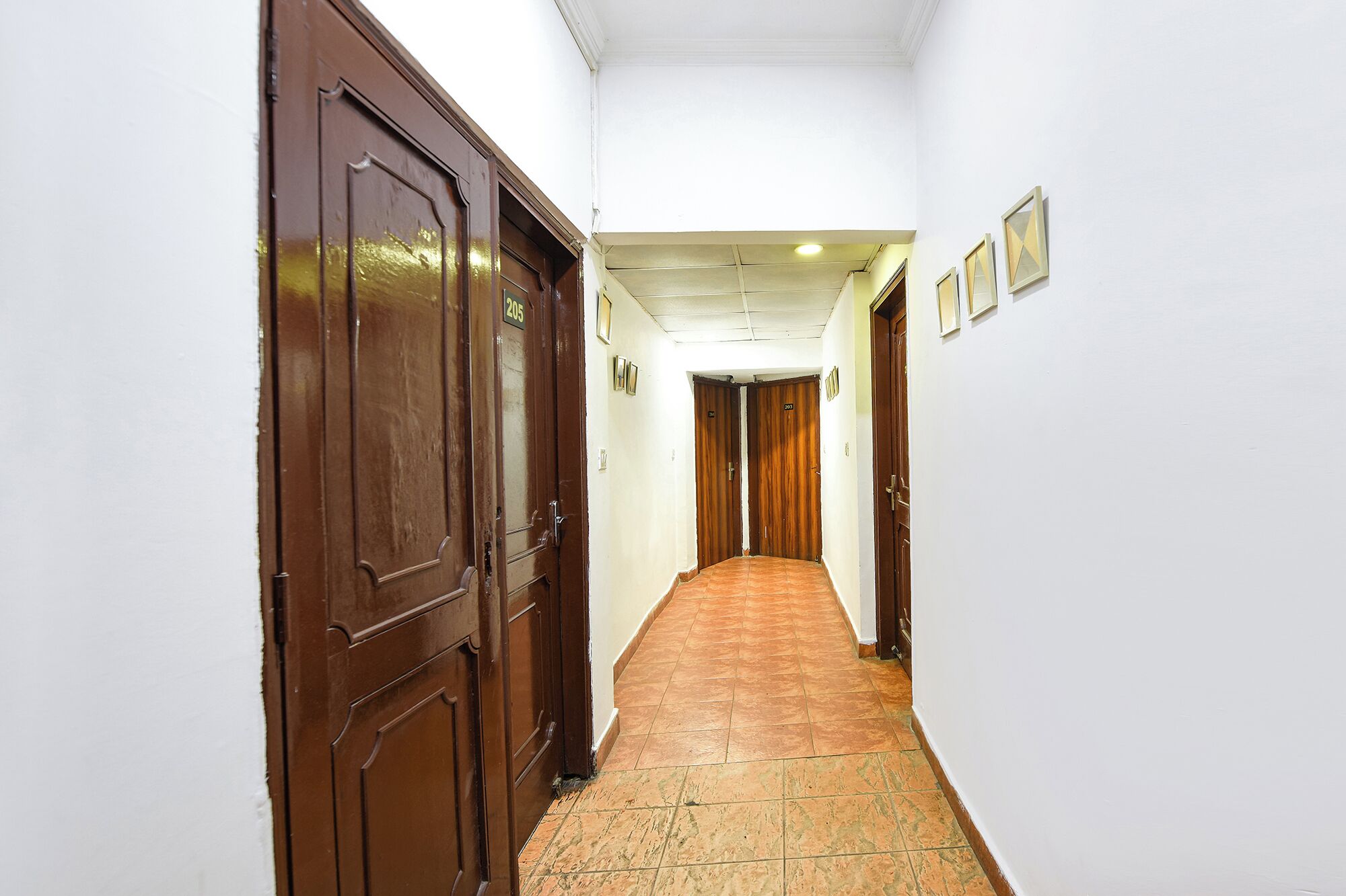 A hallway with two wooden doors, each marked with a number. The walls are white, and the floor is tiled.