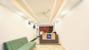 A reception area with a reception desk labeled 'Via,' a green sofa, a ceiling fan, and a tiled floor. - Via Krishna Residency - Nr. Nehru Place Metro (New Delhi)