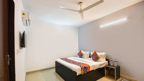 A bedroom with a bed, a nightstand, a glass table, a ceiling fan, and a wall-mounted TV. - Via Krishna Residency - Nr. Nehru Place Metro (New Delhi)