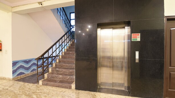 Eine Marmortreppe führt zu einem Aufzug, dessen Wand links schwarz und links daneben blau gefliest ist.