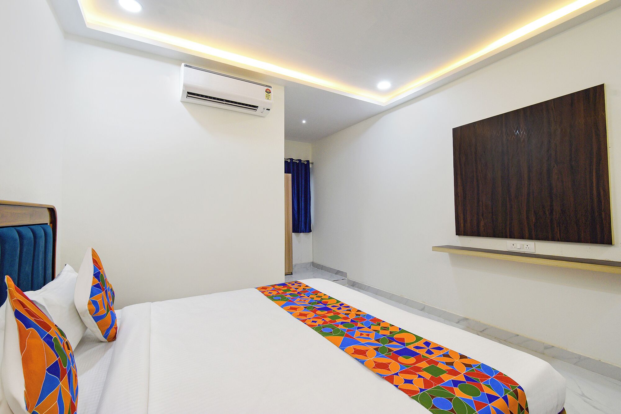 A hotel room with a bed, an air conditioner, a shower curtain, and a wooden panel on the wall.