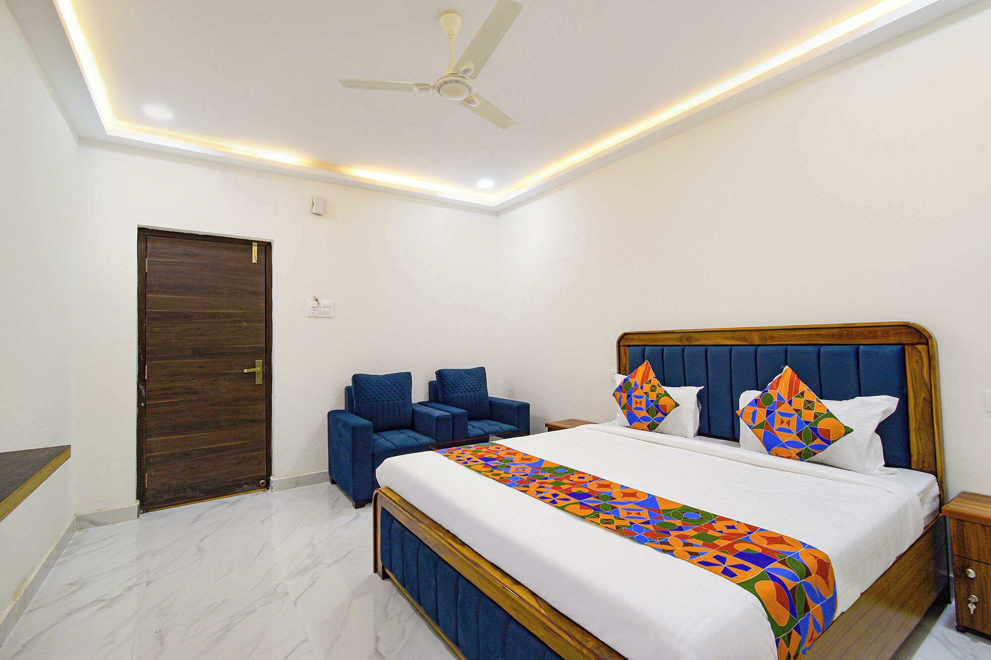 A bedroom with a bed, a ceiling fan, a wooden door, and a blue armchair.