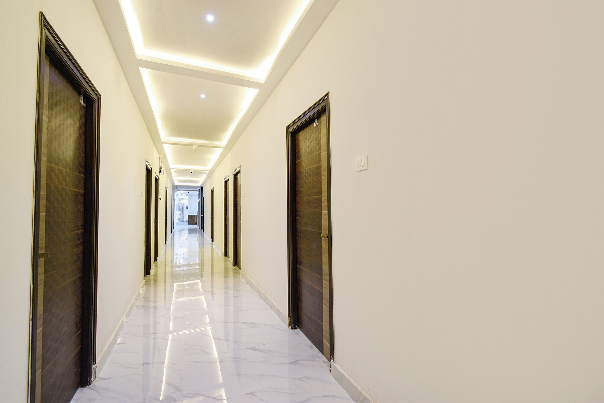 A long, narrow hallway with a shiny, reflective floor and dark wooden doors on both sides.