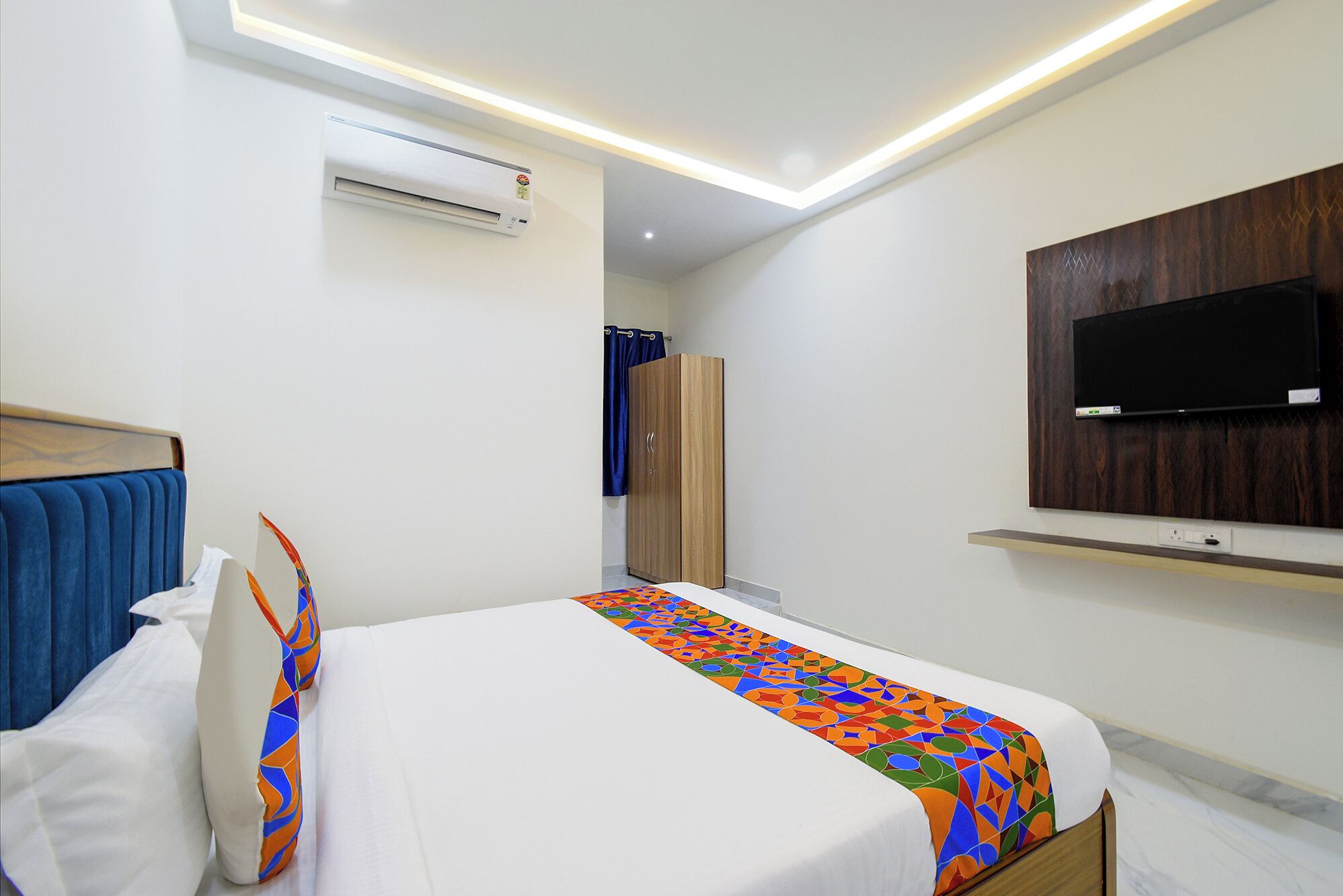 Una camera d'albergo con un letto, un condizionatore, un armadio, una televisione montata a parete e una luce a soffitto.