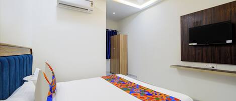 Una camera d'albergo con un letto, un condizionatore, un armadio, una televisione montata a parete e una luce a soffitto.
