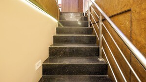 Uma escadaria com degraus de mármore preto, corrimão de metal e paredes bege.