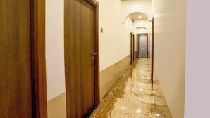 A hallway with a wooden door on the left, a marble floor, and a light-colored wall. - FabHotel Malali Residency (Mumbai)