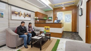 A hotel reception area with a reception desk, a waiting area with a sofa and a coffee table, and a reception staff member. - FabHotel Classic Heights - Near Yelahanka Railway Station (Bangalore)