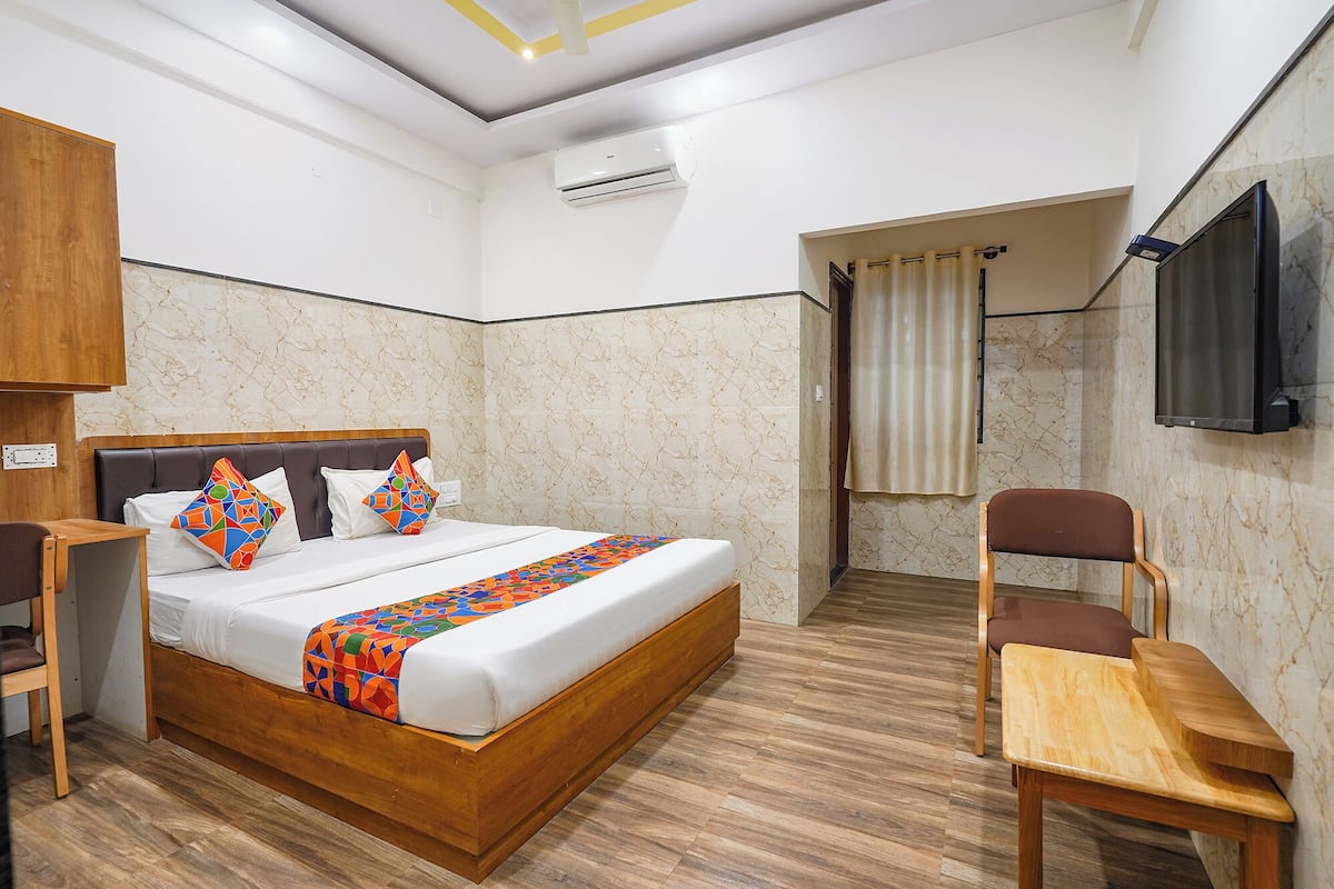 Quarto de hotel com cama, mesa de cabeceira de madeira, uma cadeira, televisão e ar condicionado.