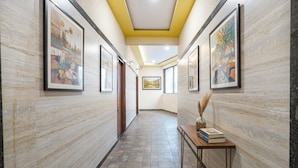 A hallway with framed artwork on the walls, a wooden bench with books, and a tiled floor. - FabHotel Classic Heights - Near Yelahanka Railway Station (Bangalore)