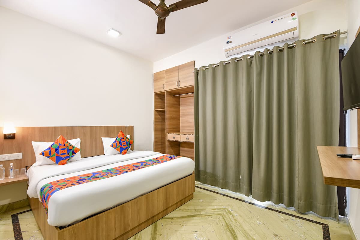 A hotel room with a bed, wooden wardrobe, a desk, and a ceiling fan.
