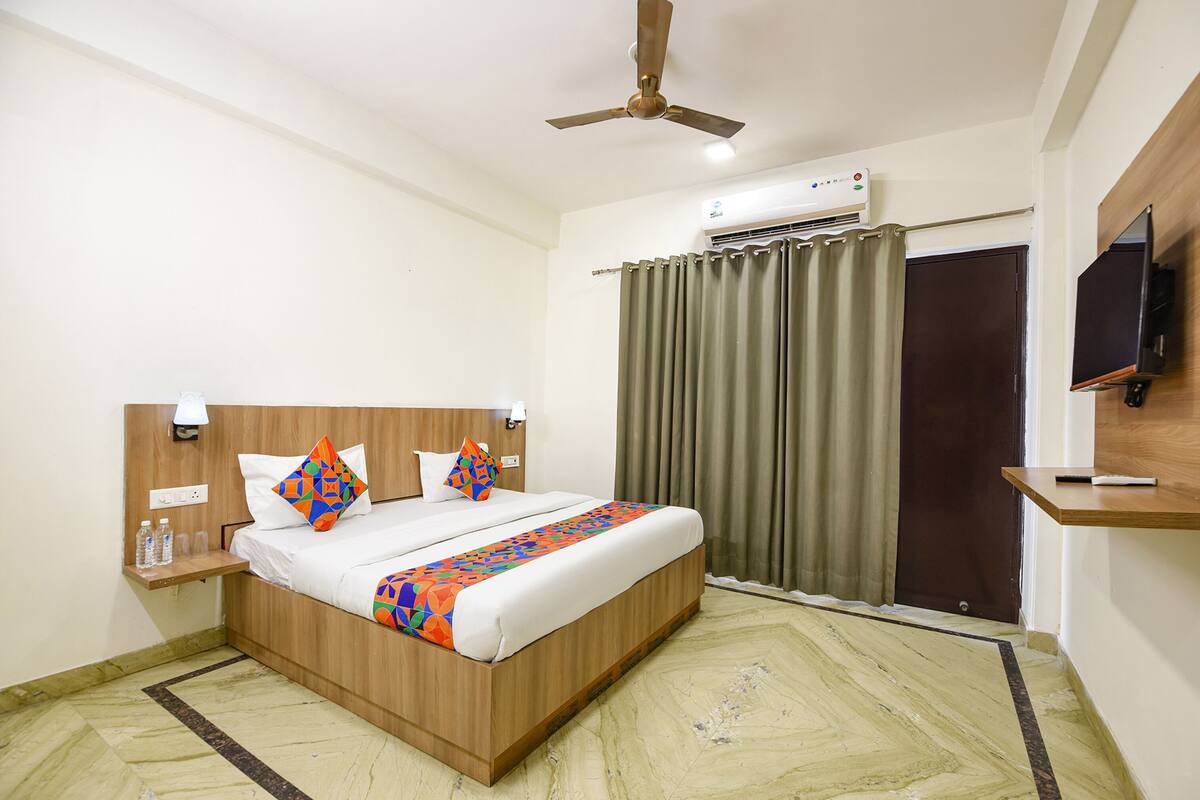 A hotel room with a wooden bed, a ceiling fan, an air conditioning unit, a TV, and a curtain.