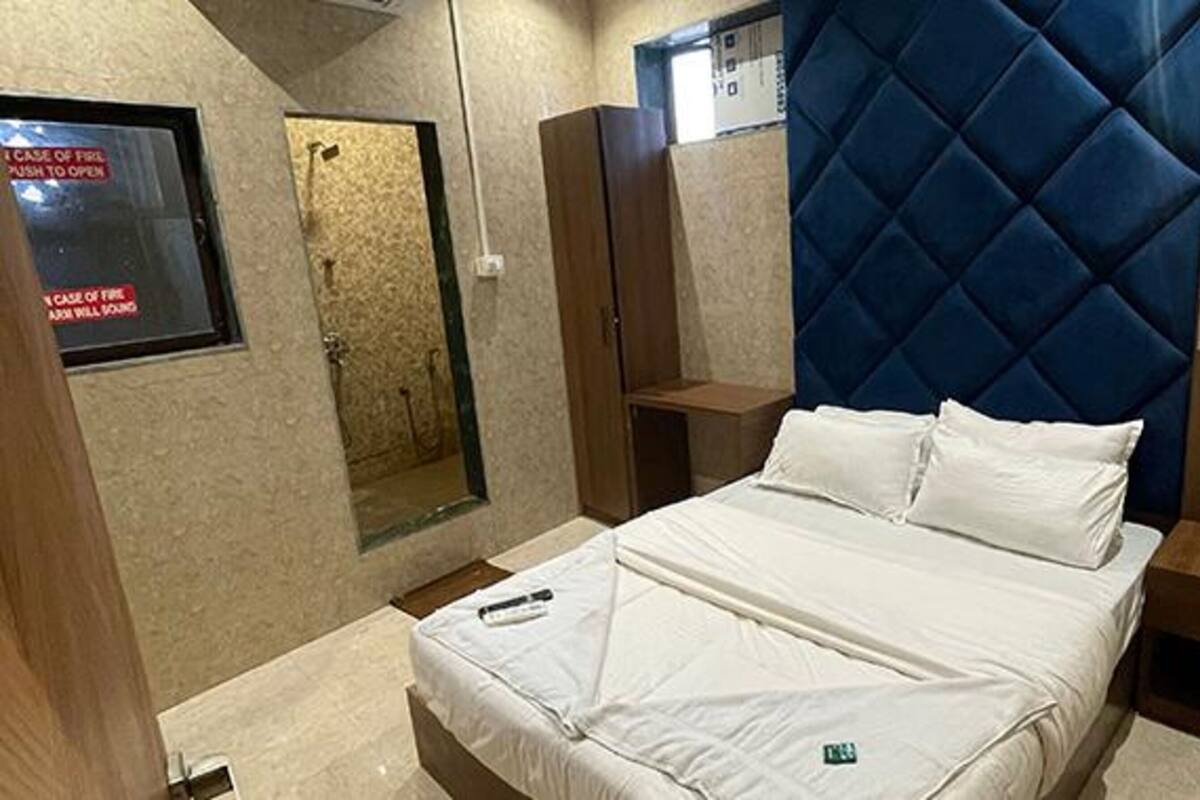 A hotel room with a bed, a small bedside table, a mirror, and a blue headboard.