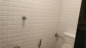 Une salle de bain avec des murs recouverts de carreaux blancs et des toilettes blanches.