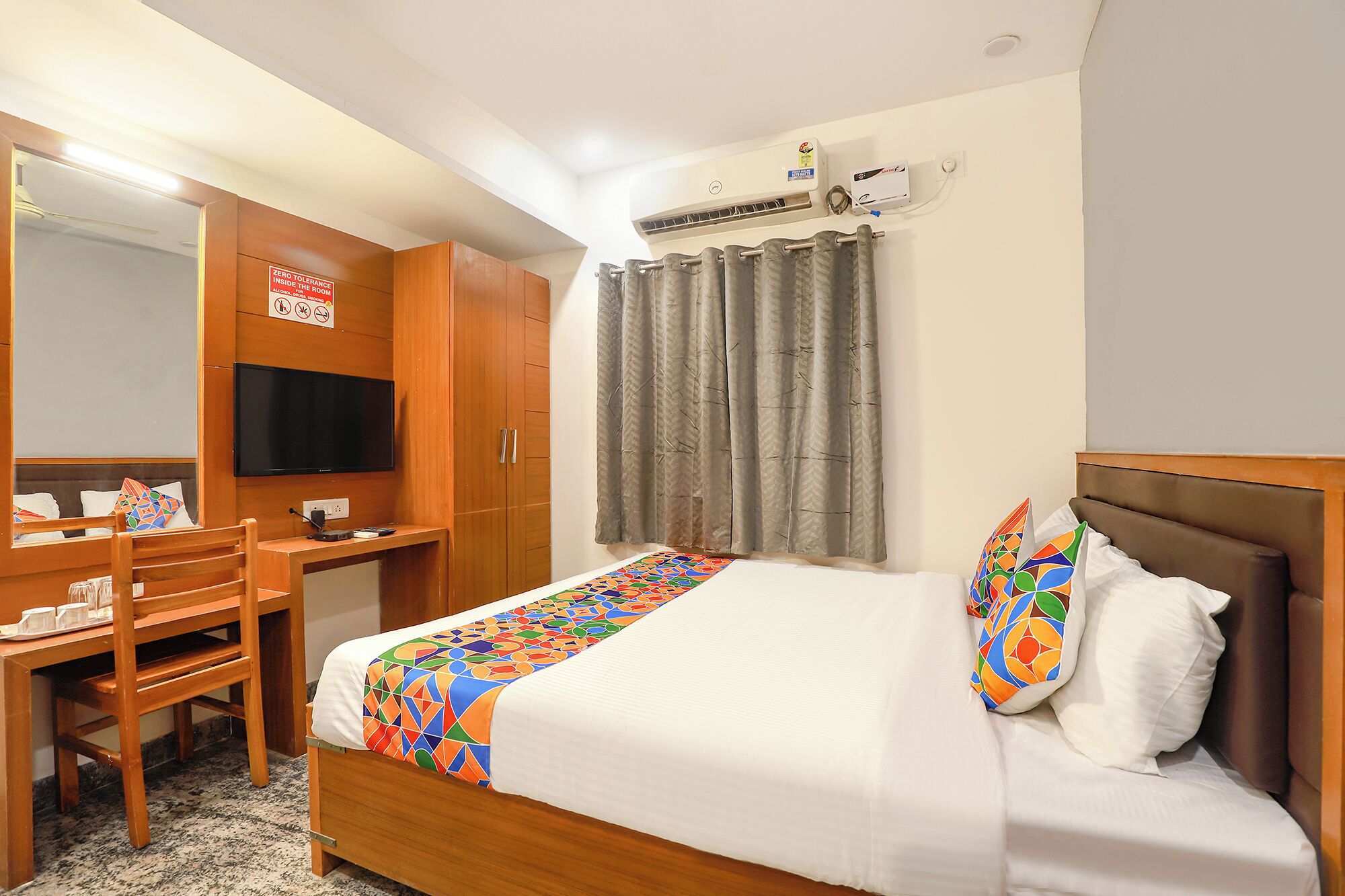 A hotel room with a bed, a desk, a chair, a television, and an air conditioning unit.