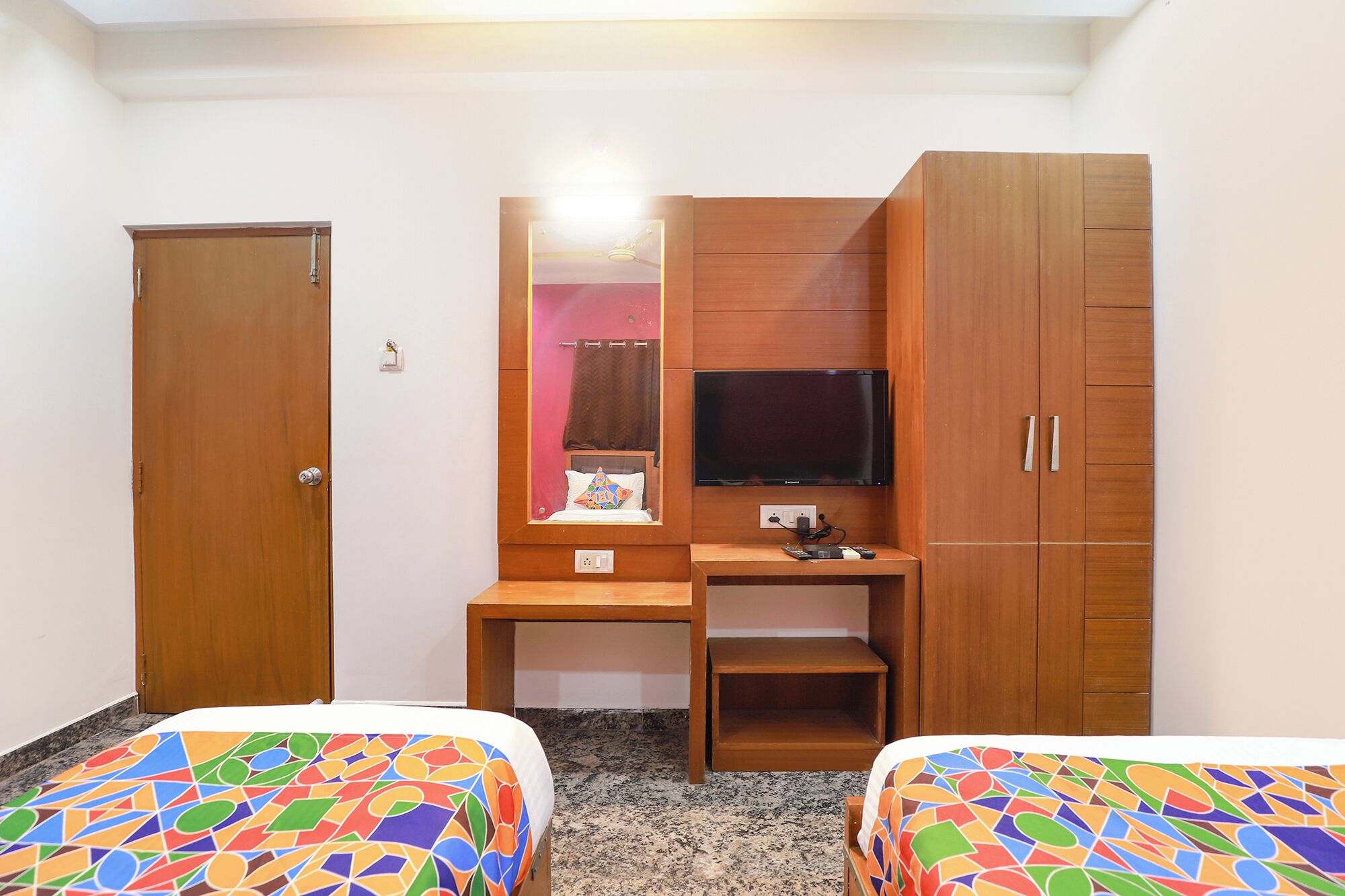 Habitación de hotel con un escritorio de madera, televisor, armario y dos camas con ropa de cama colorida.