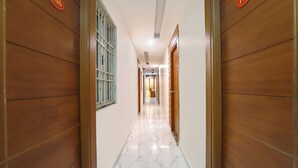 A corridor with wooden doors and a barred window, leading to a room with a tiled floor. - Fabhotel Lloyd’S Inn (Chennai)