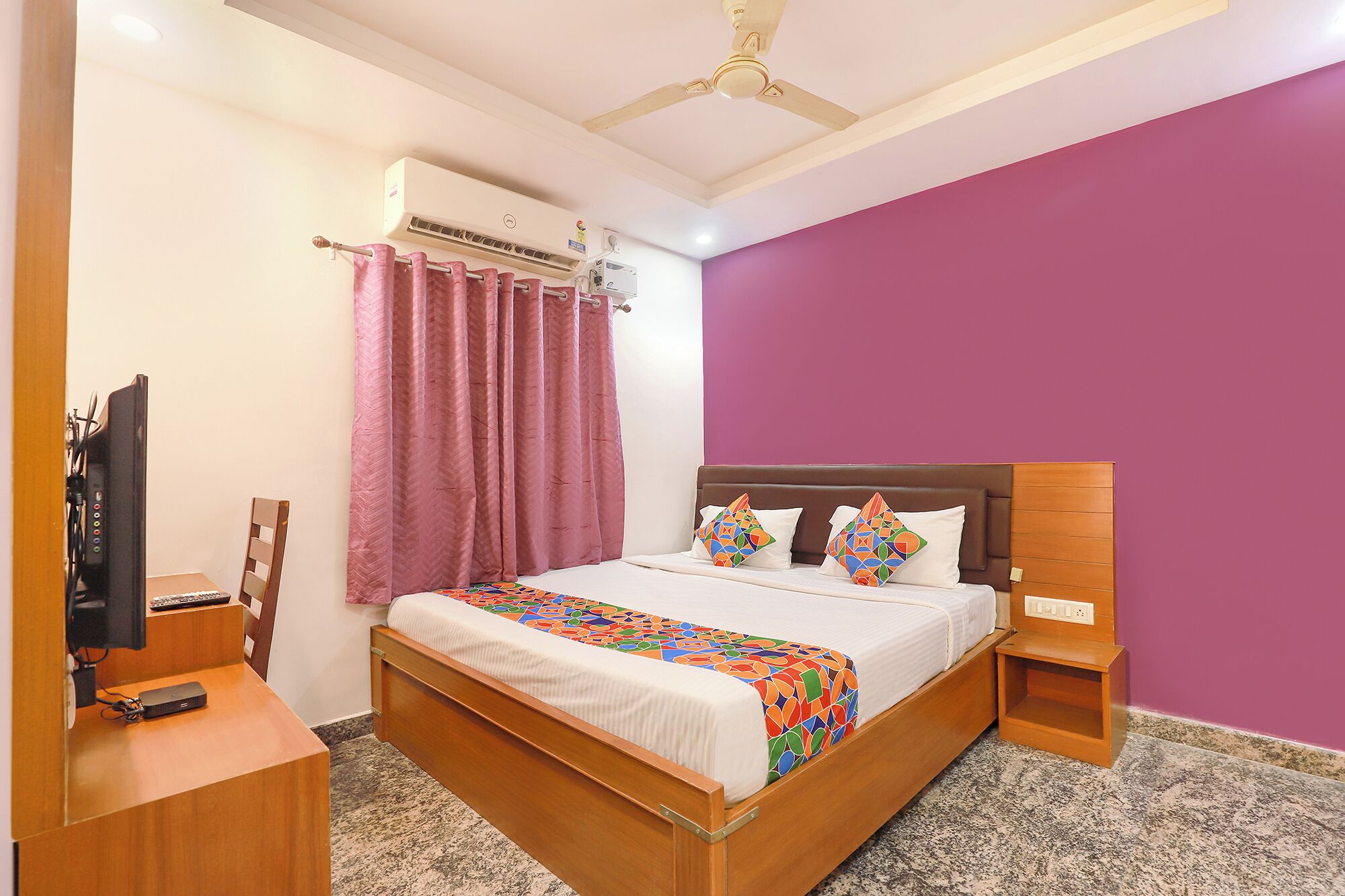 A bedroom with a bed, a desk, an air conditioner, and a ceiling fan.