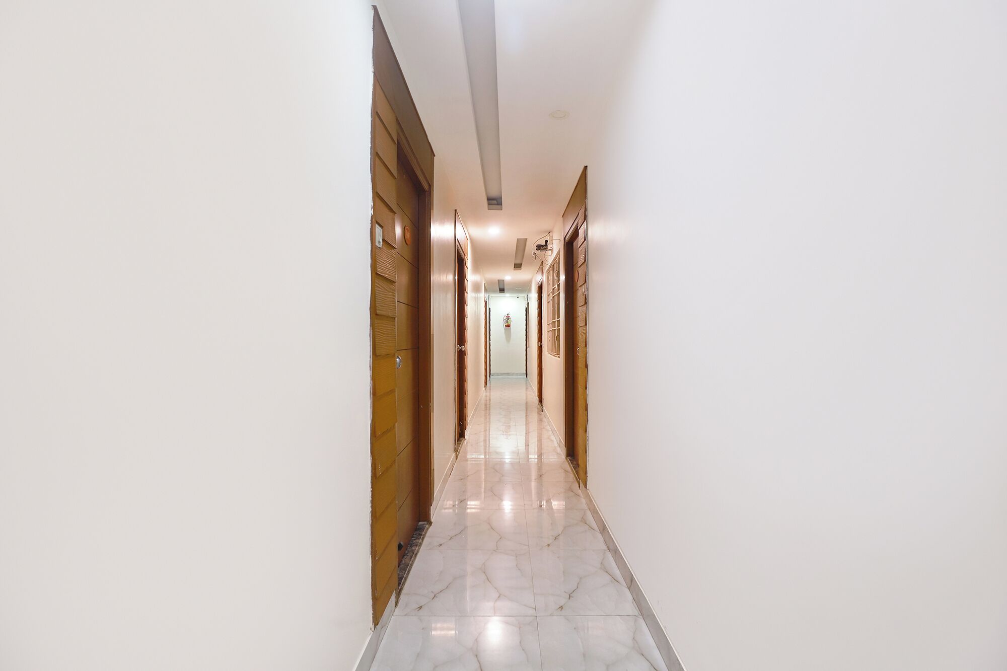 A hallway with wooden doors on the left and right, a marble floor, and a light-colored ceiling.