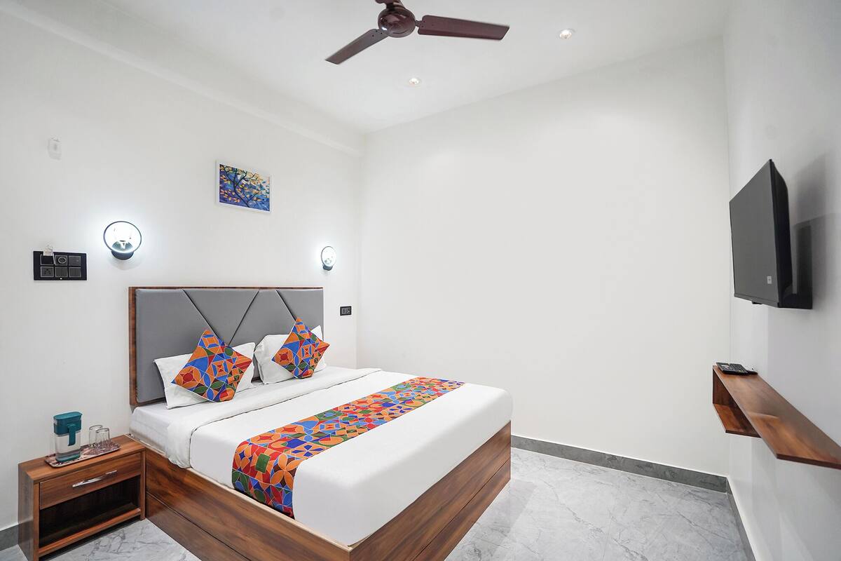 Una habitación de hotel moderna con cama, mesita de noche, ventilador de techo, obra de arte, luces fijadas en la pared y televisión.