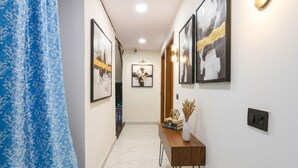 Un pasillo con obras enmarcadas en las paredes, una consola de madera con objetos decorativos y un cortinero azul estampado.