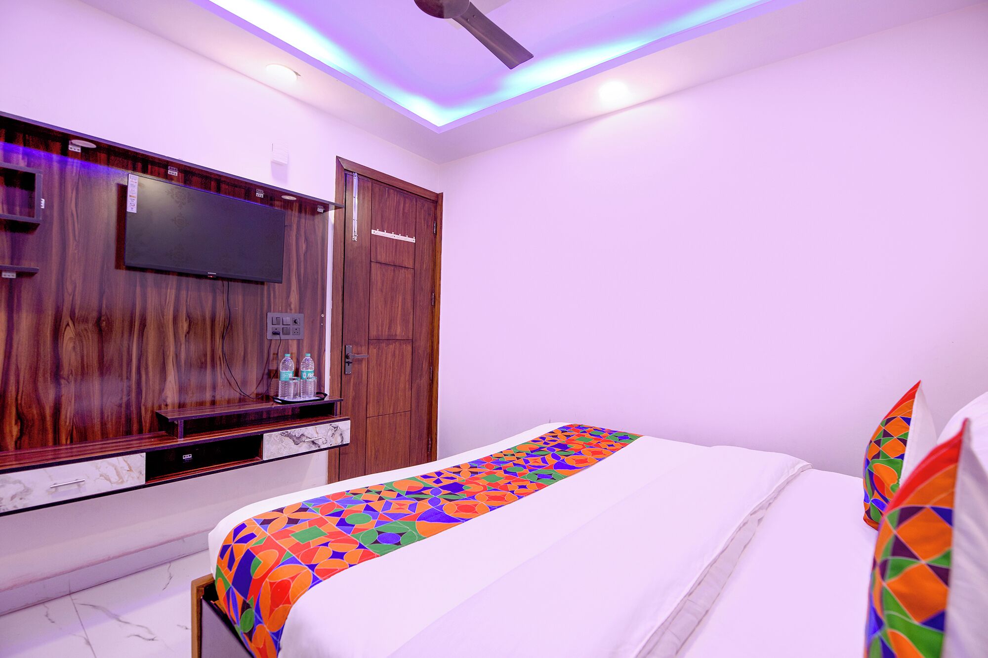 A bedroom with a bed, a wooden wardrobe, a television, and a ceiling fan.
