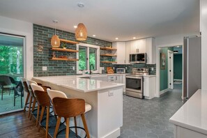 A modern kitchen with a central island, bar stools, and a dining area with a view.