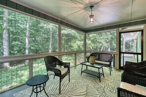 A covered porch with wicker furniture, large windows, and a ceiling light fixture.