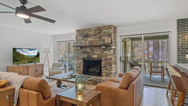 A modern living room with a stone fireplace, leather sofas, a wooden coffee table, and a television.