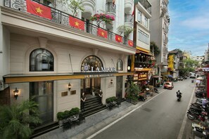 The exterior of La Mejor Indochine Hotel with a prominent entrance, outdoor seating area, and multiple balconies adorned with Vietnamese flags. - La Mejor Indochine Hotel (Hanoi)