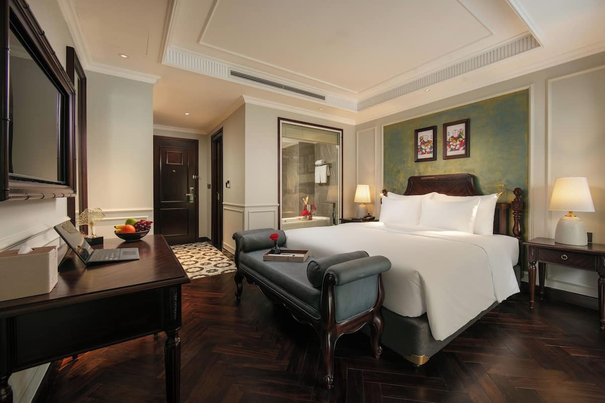 Een hotelkamer met een groot bed, een bureau met een laptop, een stoel, een tafeltje met een lamp en een spiegel.