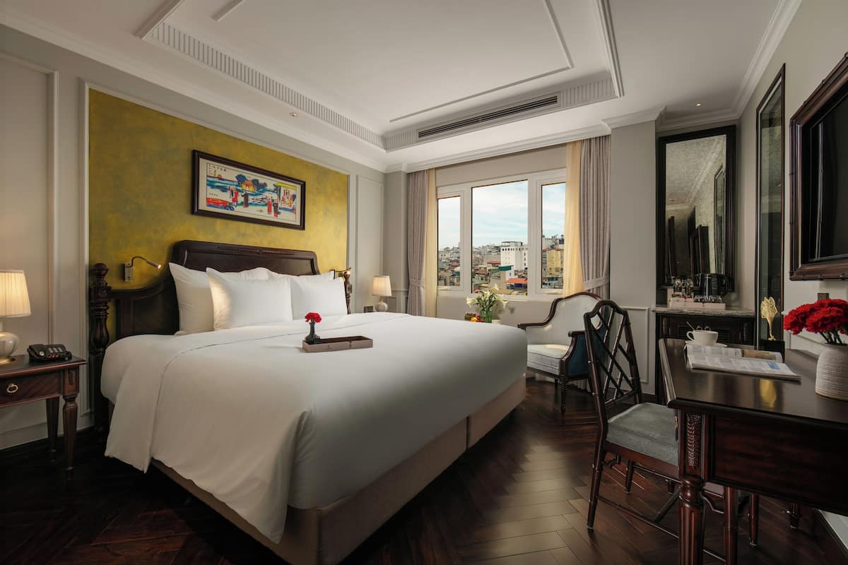 Een hotelkamer met een groot bed, een bureau, een stoel en uitzicht op de stad.