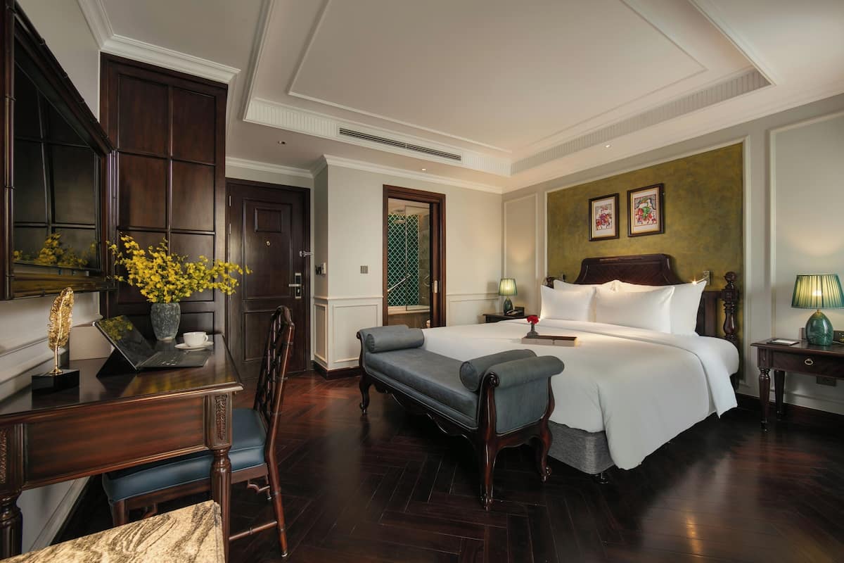 Een hotelkamer met een groot bed, een bureau met een laptop, een stoel en een bijzettafeltje met een lamp.