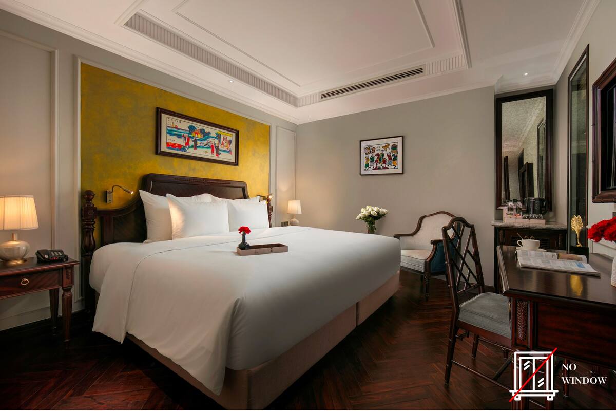 Een hotelkamer met een groot bed, twee nachtkastjes met lampen, een bureau met stoel en kunstwerken aan de muur.