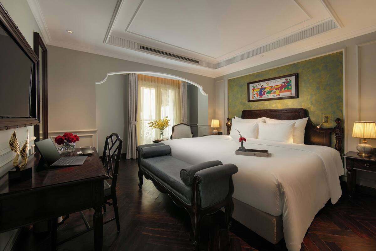 Een hotelkamer met een groot bed, een bureau met een laptop, een stoel en een nachtkastje met een lamp.