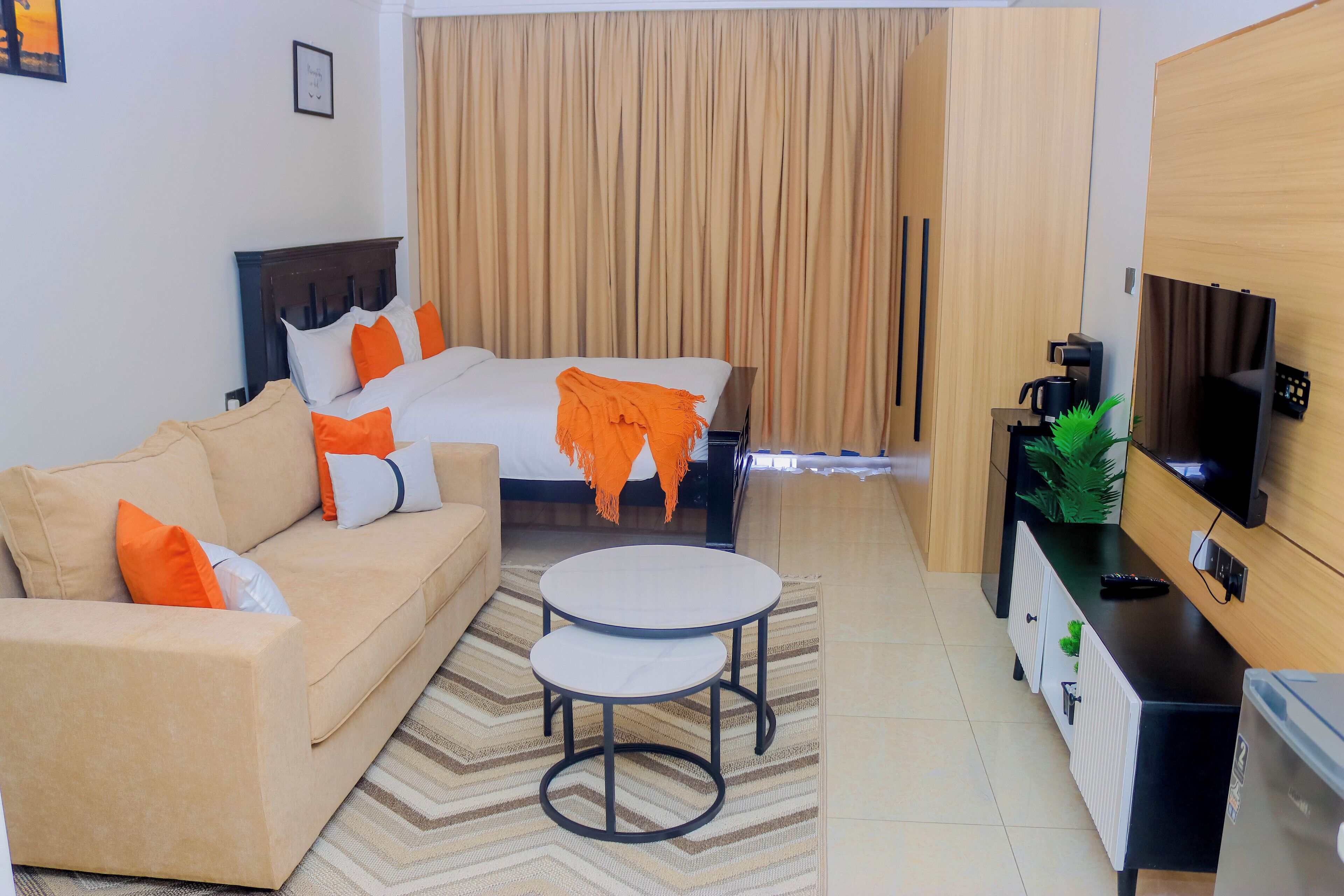 A modern hotel room with a bed, sofa, coffee table, TV, and a minibar.