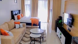 Une chambre d’hôtel avec un lit, un canapé, une machine à café, une télévision et une plante.