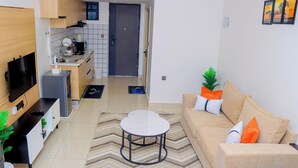 A modern living room with a sofa, coffee table, TV, and kitchen in the background. - Idlyllic Nest bed & breakfast Ruaka with AC, WiFi, fitness room,free parking (Ruaka)