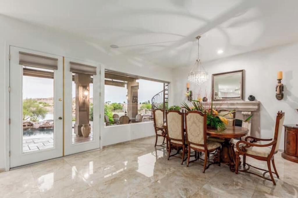 A spacious dining area with a marble floor, a chandelier, and a view of a pool through glass doors.