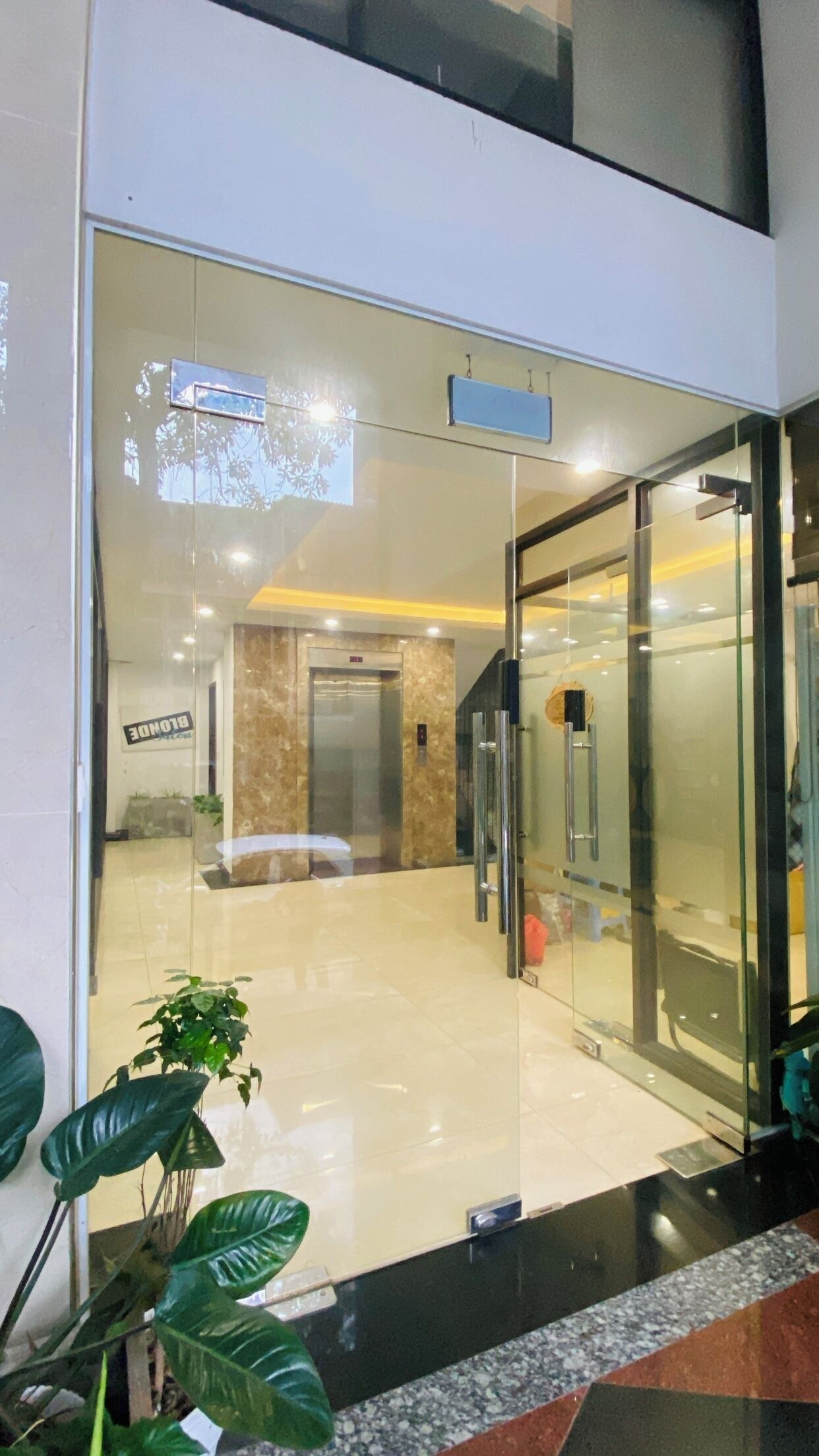 A modern building entrance with a glass door, a signboard, and a potted plant.
