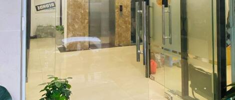 A modern building entrance with a glass door, a signboard, and a potted plant.
