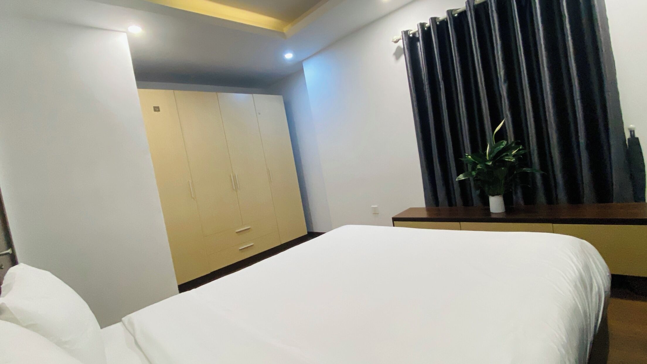 A bedroom with a bed, a wardrobe, a bedside table, and a potted plant.