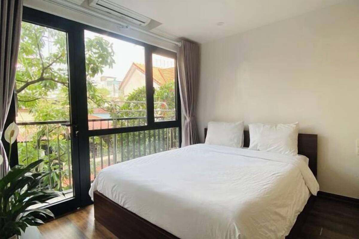 A hotel room with a large bed, a sliding glass door to the outside, and a potted plant.