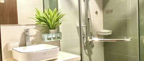 A modern bathroom with a glass-enclosed shower, a white sink, a potted plant, and a mirror.