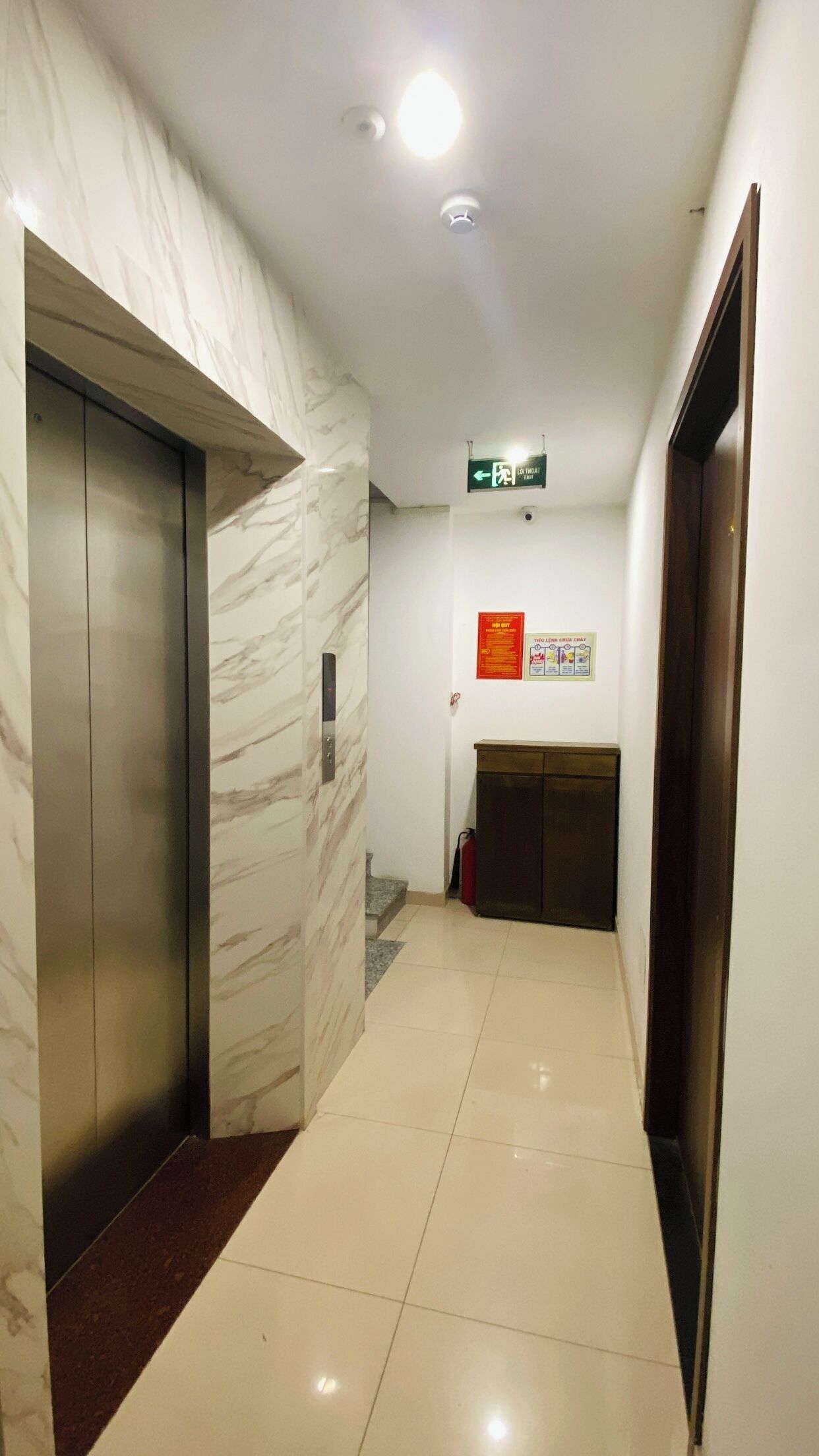 A hallway with marble walls, an elevator, a fire alarm, and a sign indicating an exit.