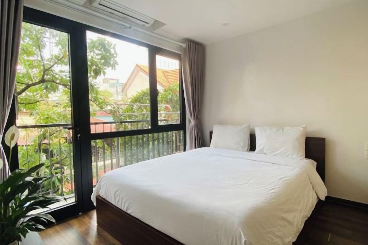 A hotel room with a large bed, a sliding glass door to the outside, and a potted plant.