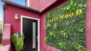 Una entrada de edificio con una puerta negra, un felpudo y una pared cubierta de follaje verde con el texto "Hollywood D" en amarillo.