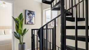 Una escalera con barandas negras, una planta en maceta y una obra enmarcada en la pared.