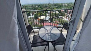 Un balcón con una mesa redonda y dos sillas, con vista a un paisaje urbano con edificios y áreas verdes.