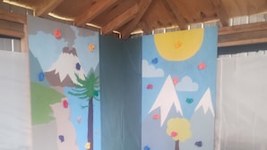 A room with a blue padded play area, wooden ceiling beams, and colorful wall decorations including mountains, trees, and clouds.